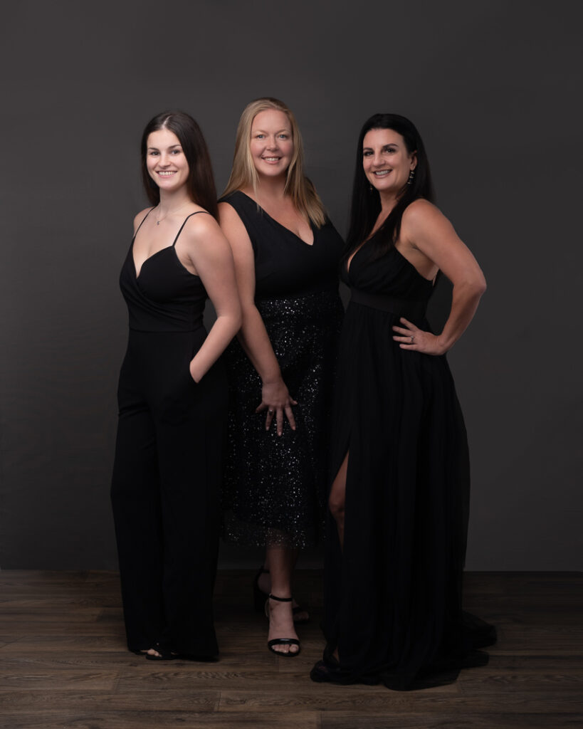 three ladies standing together wearing back and representing their company in a glamourous coworker photo